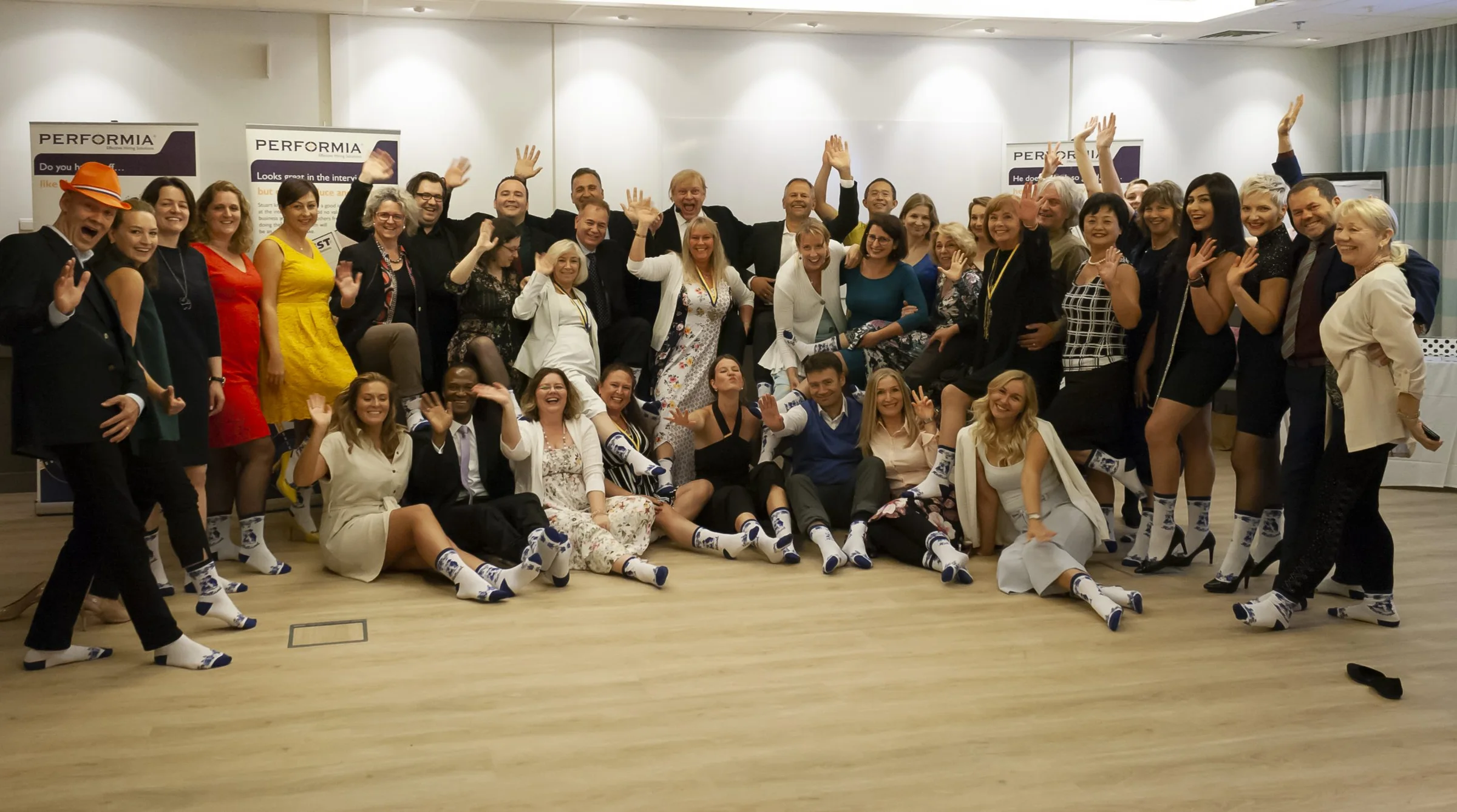 A large group of Performia people smiling and waving at the camera